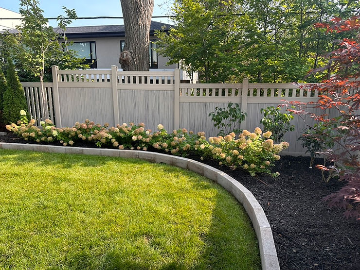 Horvath Landscapes front yard landscape with a curved stone garden border, green lawn, hydrangea planting, privacy fence, and layered ornamental trees and shrubs.