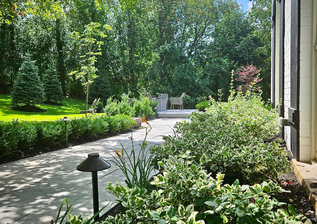 Side yard walkway with natural stone paving, lush green plantings, and mature trees enhancing the woodland property.
