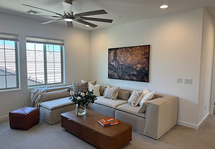 Modern living room fully stagex in Desert Ridge includes large sectional, oversized wall art, fluted oak coffee table and faux gardenia bouquet.