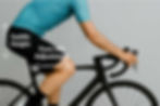 Cyclist on a black bike with a teal jersey showing an arrow and writing for saddle height and one for fore-aft saddle adjustment in a bike fit