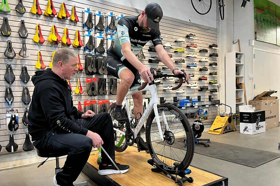 John Hughes of 90+ Cycling performing a professional bike fitting with a cyclist in front of a wall of saddles