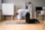 Man with dress shirt and pants on a yoga mat in an office performing the cat-cow stretch in increase spinal mobility and decrease lower back pain in cycling