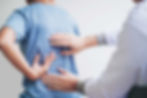 Physical therapist palpating a mans back to find the lower back pain area for treatment