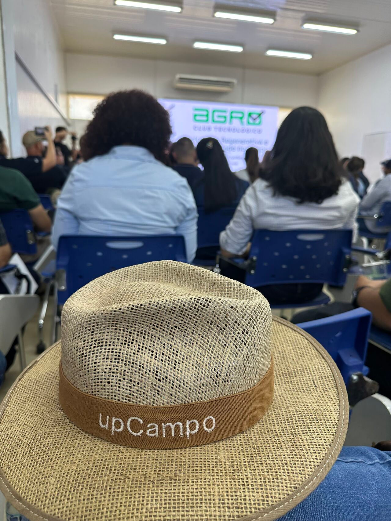 Um chapéu escrito upCampo em uma sala de auditoório com pessoas no fundo.