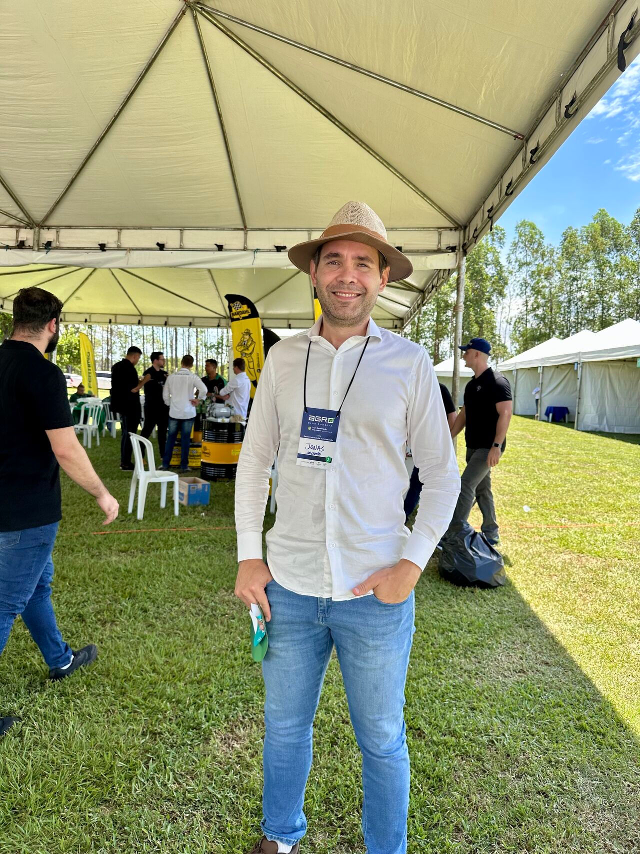 Homem de chapéu no ambiente externo do evento com pessoas no fundo