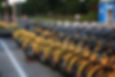 A row of yellow bicycles stand on the sidewalk, ready to be ridden.