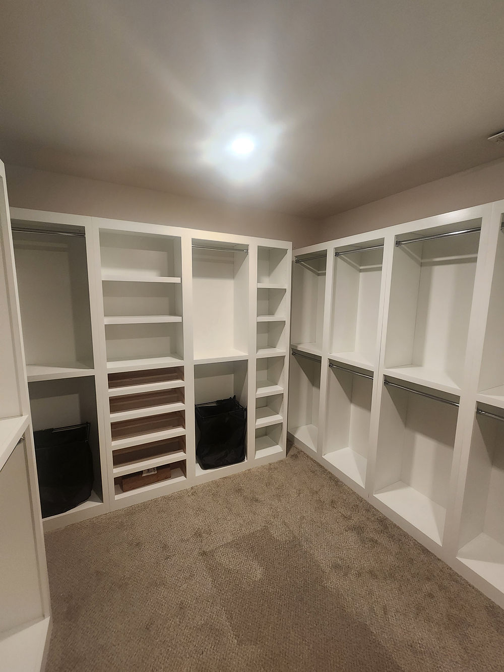 White closet components with shelves and hanging rods, drawer bank, and integrated black clothes hampers