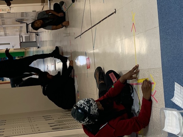 Students measuring and exploring geometric lines on a school hallway floor