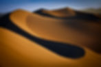 Golden sand dunes at sunrise in Death Valley National Park, showcasing sweeping curves, dramatic light, and deep shadows.