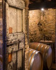 A rustic wooden door leading into a traditional wine cellar in Tuscany, Italy, featuring oak wine barrels, historic stone walls, and an authentic Italian winery interior.