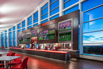 Club lounge bar at Raymond James Stadium in Tampa, Florida, featuring a long modern bar, large video displays, floor-to-ceiling glass windows, contemporary seating, and premium hospitality design.