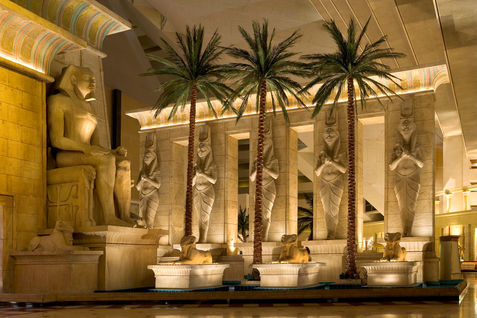 Interior of the Luxor Hotel & Casino lobby in Las Vegas, Nevada, featuring Egyptian-inspired statues, palm trees, monumental architecture, and warm architectural lighting.
