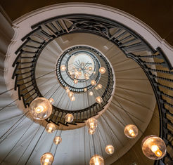 Looking upward through the spiral staircase at Heal's department store in London, England, showcasing elegant architectural curves, hanging globe lights, and a dramatic circular composition.
