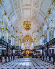 Interior of St. Clement Danes Church in London, England, showcasing white vaulted ceilings, gold architectural details, chandeliers, and the historic nave.