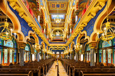 Interior of the Jerusalem Synagogue in Prague, Czech Republic, featuring colorful Moorish Revival architecture, ornate chandeliers, decorative arches, rows of wooden pews, and a richly detailed central sanctuary.