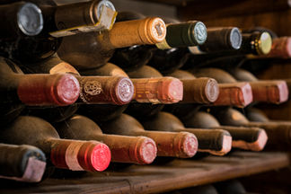 Bottles of aged wine stored on wooden racks in a traditional wine cellar in Tuscany, Italy, featuring vintage labels, corks, and a warm rustic atmosphere.