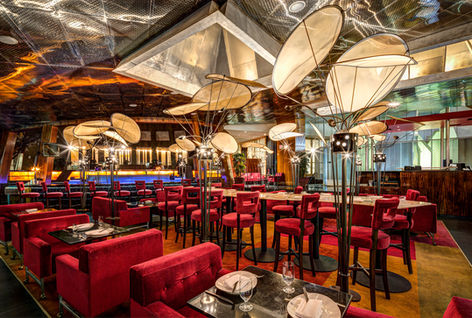 Interior of a contemporary restaurant at Mandalay Bay Resort in Las Vegas, Nevada, featuring modern lighting fixtures, red upholstered seating, elegant dining tables, and upscale hospitality design.
