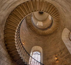 Looking upward through the spiral staircase inside St. Paul's Cathedral in London, England, showcasing sweeping stone steps, circular symmetry, and historic architecture.