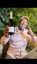 Thaddeus Buggs smiling while holding a bottle of Champagne, celebrating with enthusiasm in an outdoor setting, showcasing his passion for fine wine and memorable wine experiences.