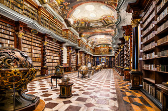 Interior of the Klementinum Baroque Library in Prague, Czech Republic, featuring ornate Baroque architecture, richly decorated frescoed ceilings, towering historic bookshelves, antique globes, and an elegant checkerboard marble floor.
