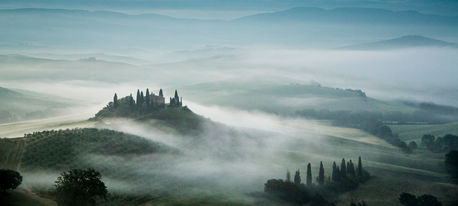 Belvedere Farm in Tuscany, Italy, surrounded by rolling hills and morning mist, featuring a hilltop farmhouse, cypress trees, layered fog, and the serene beauty of the Tuscan countryside at sunrise.