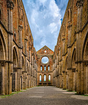 Interior of the Abbey of San Galgano in Tuscany, Italy, featuring soaring Gothic stone arches, roofless ruins, symmetrical architecture, and an open sky above.