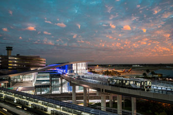 SkyConnect station at Tampa International Airport in Tampa, Florida, photographed at twilight, featuring the elevated automated people mover, modern glass architecture, airport terminals, and a colorful sunset sky.