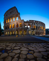 The Colosseum in Rome, Italy, photographed at blue hour with illuminated arches, ancient stone architecture, and the historic cobblestone foreground.