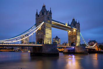 Tower Bridge illuminated at twilight over the River Thames in London, England, with long exposure reflections, blue hour sky, and historic architecture.