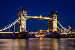 Tower Bridge illuminated at night over the River Thames in London, England, with long exposure reflections on the water and a deep blue evening sky.