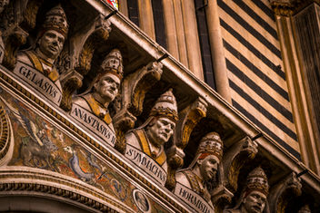 Carved statues of the popes inside Siena Cathedral in Siena, Tuscany, Italy, featuring ornate Gothic architecture, colorful marble walls, and intricate decorative details.