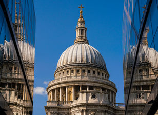 St. Paul's Cathedral in London, England, framed by reflections in modern glass buildings, showcasing the contrast between historic architecture and contemporary city design.