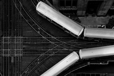Black-and-white aerial photograph of Chicago's elevated 'L' trains navigating intersecting tracks in downtown Chicago, Illinois, showcasing geometric railroad patterns and the city's iconic rapid transit system.