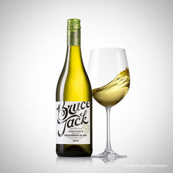 Studio photograph of a bottle of Bruce Jack Chardonnay beside a wine glass filled with white wine, featuring a clean white background, elegant lighting, and contemporary wine product photography. Photograph by Karen Bengall.
