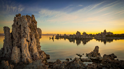 Tufa towers rising from the calm waters of Mono Lake in California at sunrise, featuring dramatic limestone formations, colorful morning skies, and mirror-like reflections.