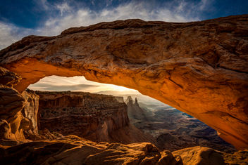 View through Mesa Arch in Canyonlands National Park, Utah, at sunrise, featuring the glowing sandstone arch framing rugged red rock canyons, towering buttes, and dramatic desert scenery.