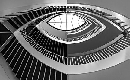 Black-and-white photograph looking up through the Grand Staircase at the Art Institute of Chicago in Chicago, Illinois, featuring sweeping curved staircases, geometric symmetry, and a skylight overhead.