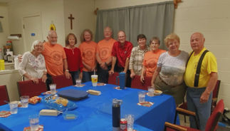 old people standing behind blue table wearing matching shirts