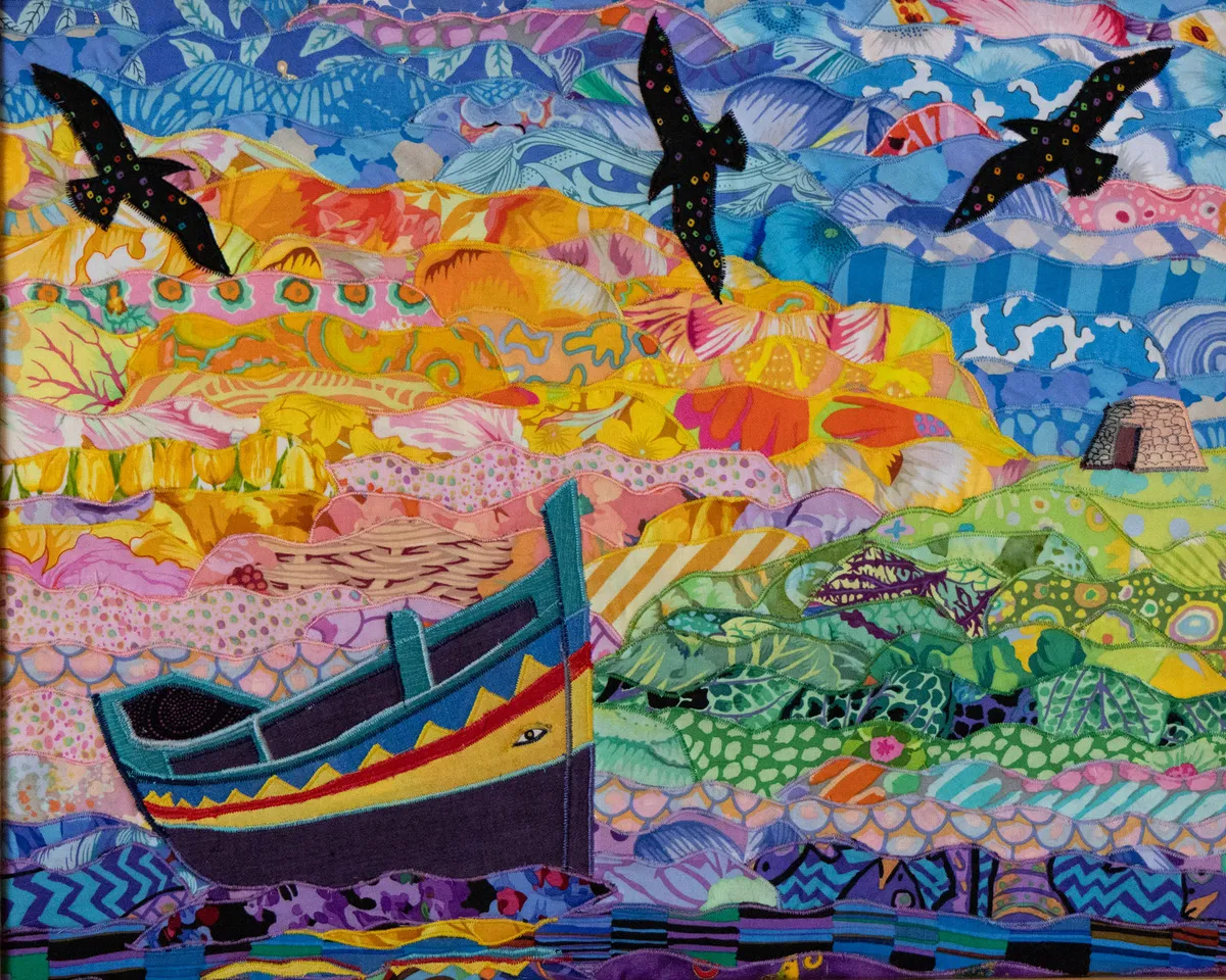 Textile art by Anna Wright depicting a large, detailed Luzzu boat in front of yellow cliffs and a blue-and-white patterned sky.