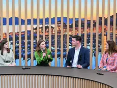 Four panelists seated on a stage, speaking into microphones during a conference session with a large screen in the background.