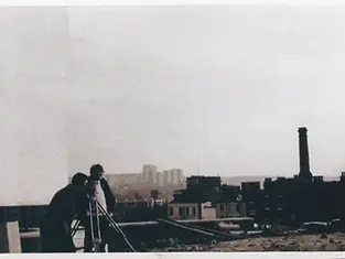 A black and white AI-generated image of Prime Minister Harold Wilson standing on a railway platform at Sheffield Pond Street Station in June 1970. He is wearing his iconic Gannex raincoat, holding a pipe in one hand and a briefcase in the other.