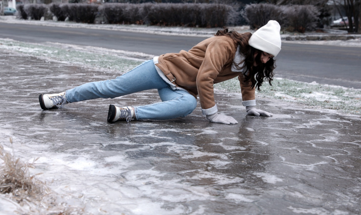 Young woman trying to stand up after falling on slippery icy pavement