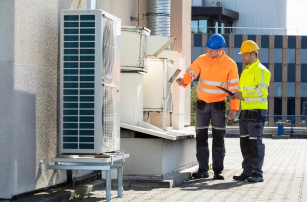 Two Technicians Men Wearing Safety Jackets Checking Air Conditioning Unit On Building Rooftop
