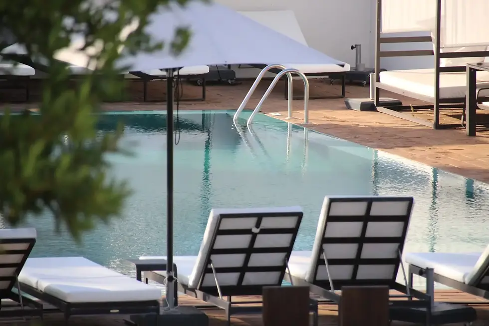 Poolside scene with empty lounge chairs under umbrellas, next to a calm pool with a ladder. Bright, sunny atmosphere; tranquil vibe.