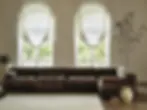 Boutique Hotel Furniture in Portugal | Custom Hospitality Solutions - Brown sectional sofa in a bright room with large windows and sheer curtains. Greenery outside, potted plants and light rug inside. Minimalist vibe.