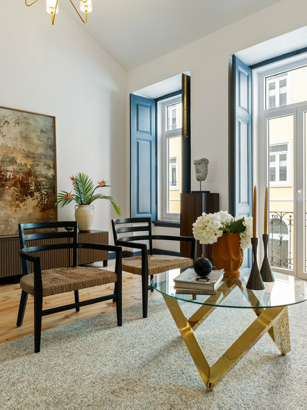 Living room in Lisbon apartment with sofa and chairs, rug, and natural light.