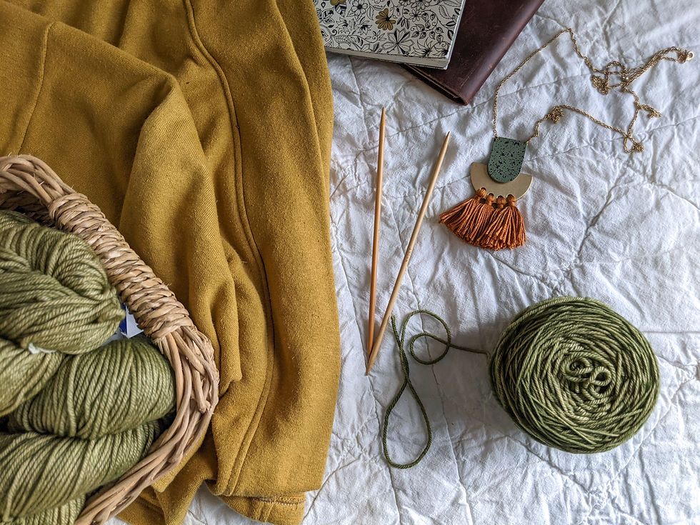A mustard hemp fleece jacket, skeins of warm olive green yarn, knitting needles, and a fast-fashion necklace with clay colored fringe.