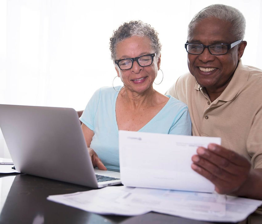 Smiling senior couple reviews paperwork with a laptop at a table
