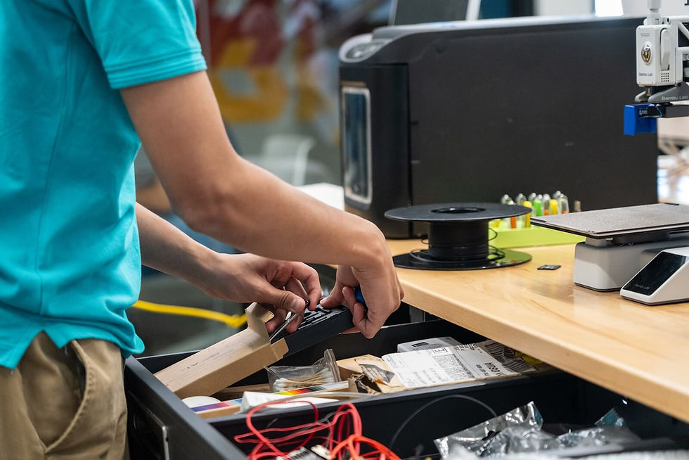 Person opening drawer with tools and supplies next to 3D printer and spool.