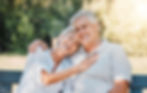 Smiling senior couple sitting on bench, enjoying sunny day. Happiness and love in the park.